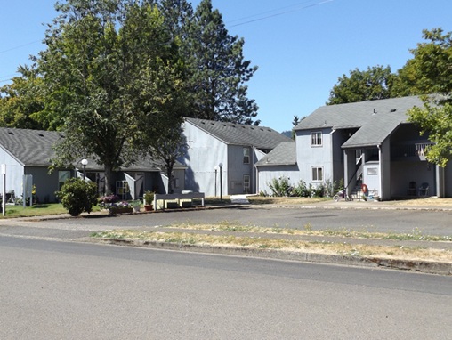 An apartment complex comprised of three buildings with a parking lot in front.