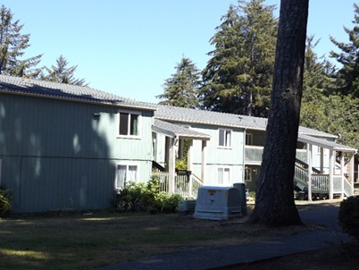 An affordable housing complex partially shadowed by trees.