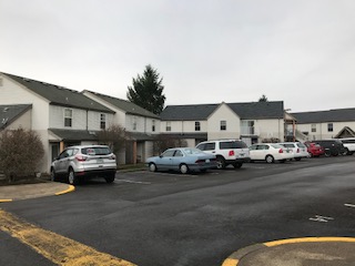 Two-story apartment buildings with paved parking in front.